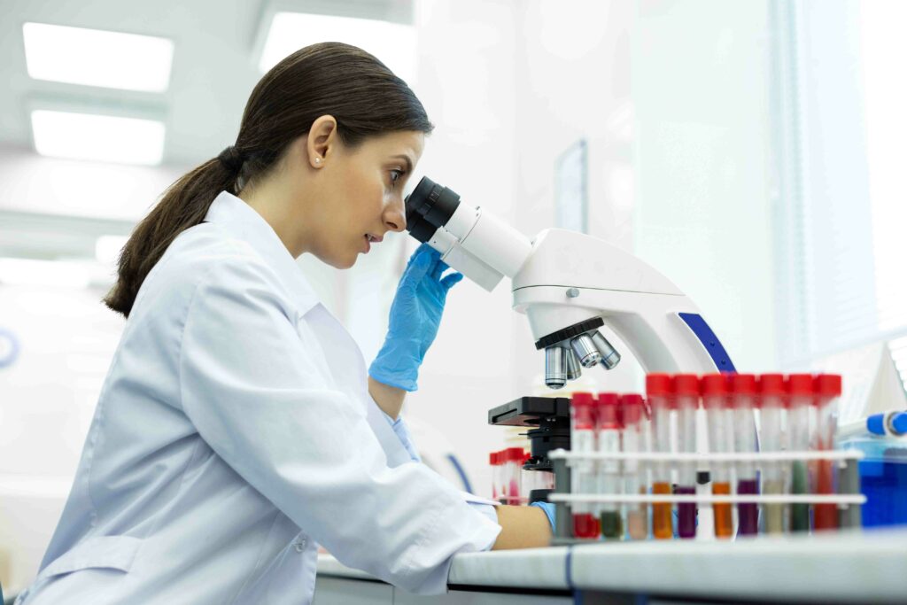 Pretty young pharmacist sitting in semi position and examining test tubes with colorful liquid