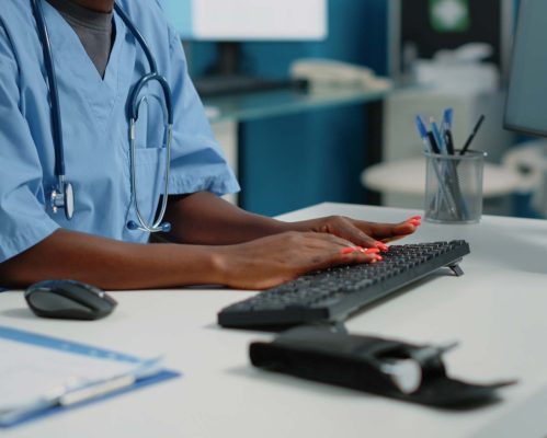 Close up of medical assistant typing on computer keyboard in cabinet for appointments with patients. Woman nurse using monitor and technology for healthcare system and reception